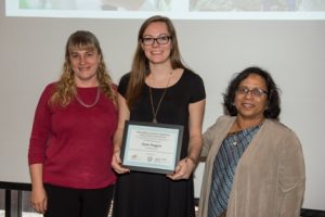 3 women with center person holding award.