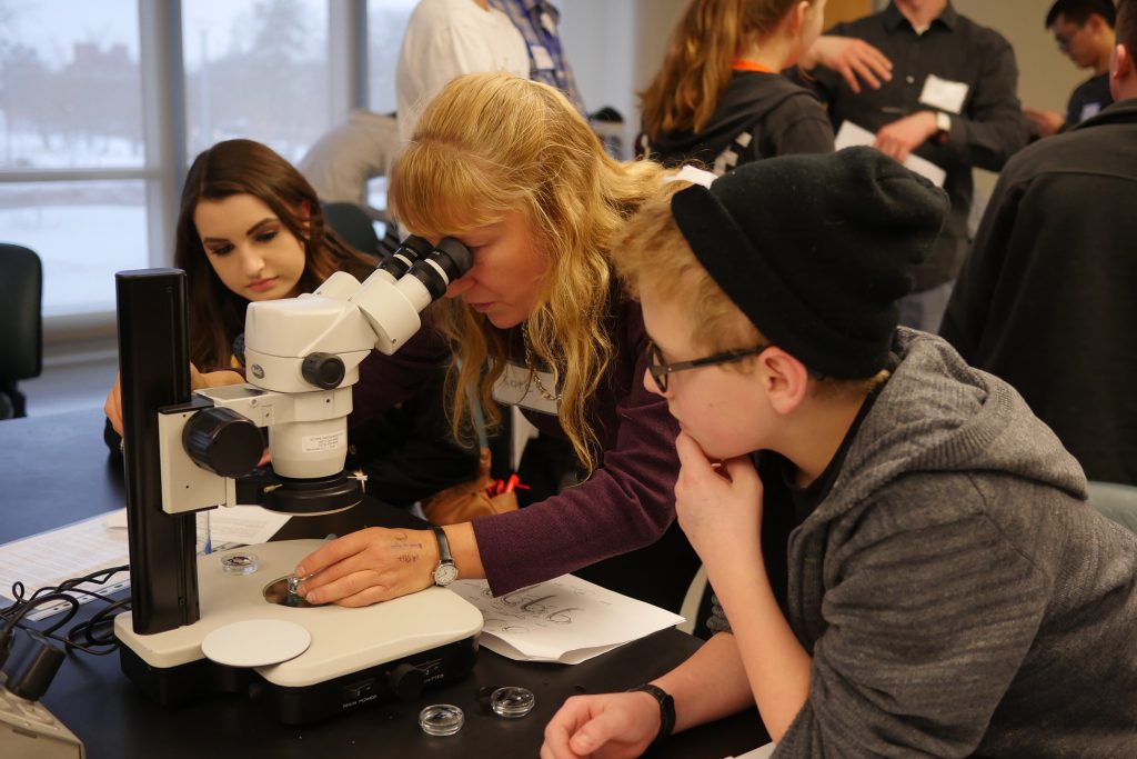 Two HS students looking on while Dr. Lewis finds a specific sample in the microscope.