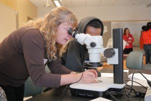 Kate Lewis finding a sample under the microscope for a HS student.