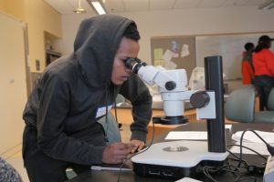 Male HS student looking into a microscope.